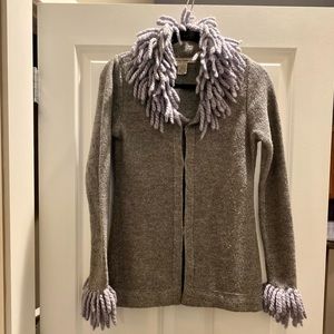 Cardigan with fringe detail on neck and sleeves. Hook clasps to close.